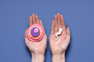 Hands with sperm cell and ovum on blue background
