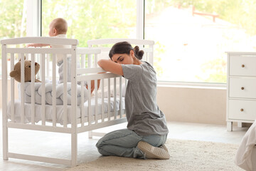 Young mother suffering from postnatal depression and her baby in crib at home