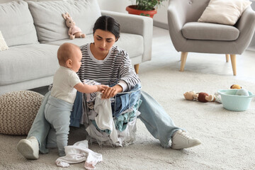 Young mother suffering from postnatal depression with dirty laundry and her baby at home