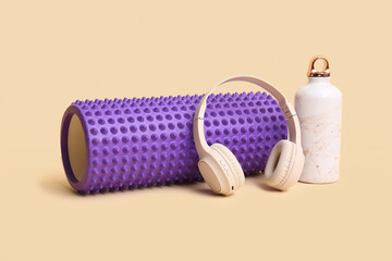 Foam roller with bottle of water and headphones on yellow background