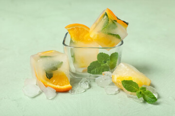 Glass bowl with slices of frozen orange in ice cubes and mint leaves on green background