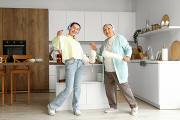 Happy young woman and her grandmother with headphones cleaning in kitchen