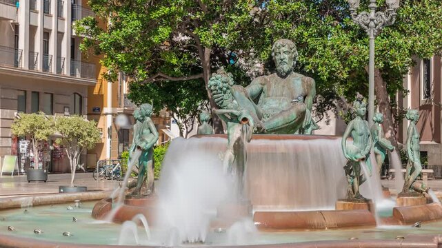 Timelapse of Plaza de la Virgen with the iconic Turia Fountain in Valencia, Spain. The Neptune statue represents the Turia River and its canals. People strolling around the square with green trees