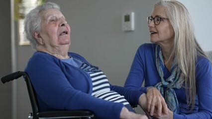 Obraz premium Warm interaction between an elderly woman and her daughter in a cozy indoor setting. They demonstrate love and care during their daily time together.