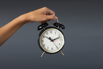 Hand Presenting Classic Alarm Clock Against Grey Background