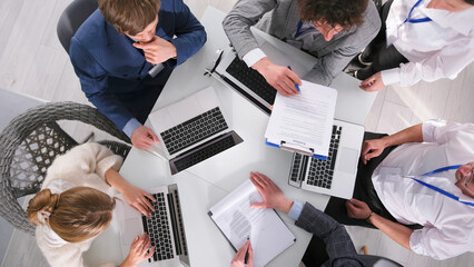 Meeting. A group of people is sitting at a table and working on laptops on the details of an important transaction, top view