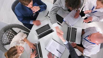 The process of concluding an important transaction, top view. A group of businessmen shake hands sitting at a table with laptops and papers