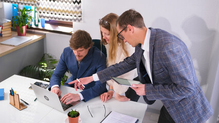 A team of professional marketers is conferring at the head's desk. Two men and a woman are looking at a laptop screen
