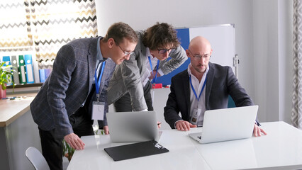 The three co-founders of the business company are carefully looking at the sales statistics on their laptop screen. A group of successful men discuss work