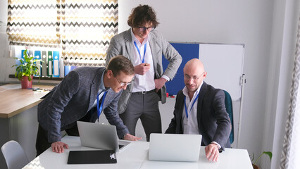Mentoring. The male consultant team is having fun looking at the laptop screen. Three men in suits and glasses are working on a project