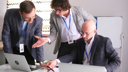Three men in suits and glasses are conferring in a conference room. Businessmen are looking at laptops and working on a common project