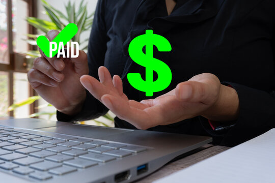A person raises their hands with the word "PAID" in green in one hand and the outline of a dollar sign in the other, next to an open laptop screen showing a check mark symbol, with an office backgroun