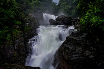 Powerful Borhill  waterfall cascading over dark rocks amidst lush green foliage.