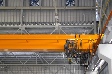 Overhead crane in factory or warehouse. Industrial machine or lifting equipment with hoist, hook and wire rope on beam girder structure for manufacturing production and freight shipping transport.