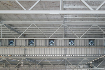 Row of ventilation fan on side wall under roof ceiling in factory warehouse. Attic insulation under roof sheet. Steel fan part of industrial building for heat air drain, air circulation. 