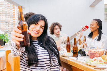 Gathering of friends singing and playing guitar, young Latin woman toasts and looking at the camera