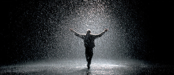 Obraz premium A man standing in the rain with his arms outstretched in a dark and dramatic monochrome scene