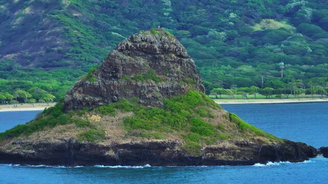 Experience breathtaking aerial views of the iconic Chinamans Hat Island located in Kualoa, Oahu, showcasing its lush greenery, tranquil waters, and stunning landscapes