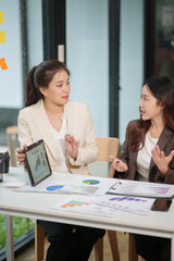 Two Asian businesswomen are sitting in a meeting, planning investment plans, business strategies. On the table are documents and graphs.