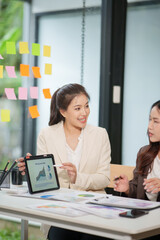 Two Asian businesswomen are sitting in a meeting, planning investment plans, business strategies. On the table are documents and graphs.
