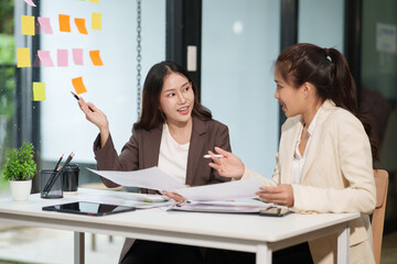 Two Asian businesswomen are sitting in a meeting, planning investment plans, business strategies. On the table are documents and graphs.