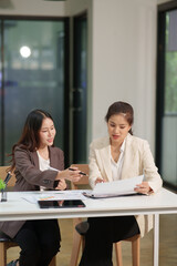 Two Asian businesswomen are sitting in a meeting, planning investment plans, business strategies. On the table are documents and graphs.
