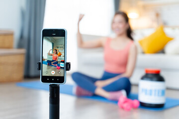Asian fitness influencer presenting whey protein during online workout at home.Asian female influencer recording online fitness video at home,introducing whey protein supplement.Concept of health care