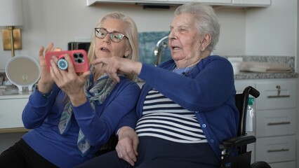 An elderly woman in a wheelchair enjoys a video chat with her daughter, both smiling and sharing memories in their cozy home environment.