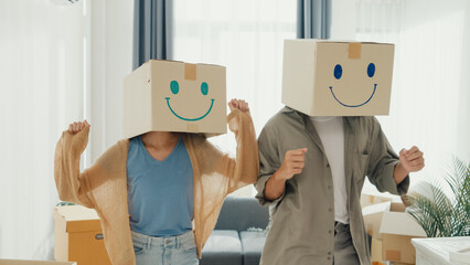 Happy Asia couple stand front of sofa couch used carton box made smiling face funny dance front of camera together in living room at new house. Husband and wife moving new house, Couple goal Concept.