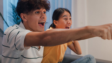 Close-up Asian new marriage couple sit on sofa excited cheering watching football sport game on television in living room at home at night. Young couple sport fans celebration online soccer on TV.