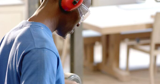 African American man in blue shirt shaping blank on lathe in shop, with gouge, copy space