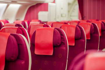 Empty Business Class Seats on a Modern Airline Cabin. A row of unoccupied airplane seats with distinctive red and purple upholstery inside a contemporary airplane, ready for passengers.