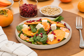 Winter salad. Fresh persimmon and pomegranate spinach salad with feta and pine nuts. Copy space