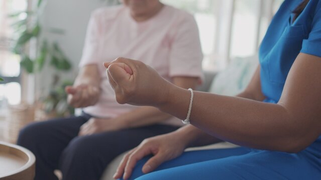 Asian health care worker giving elderly woman physiotherapy at home, home nurse, home care service concept