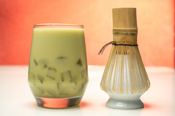 Closeup view of iced matcha green tea on the glass with a traditional bamboo brush whisk or chasen...
