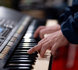 Close-up of hands playing piano keys on digital keyboard synthesizer. Musician performing on electronic instrument with selective focus on fingers and black white keys. Music production concept.
