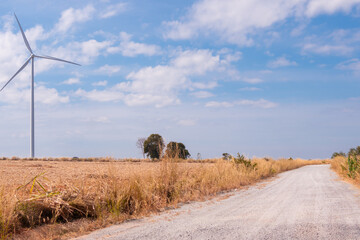 Wind turbine standing tall in a dry field under a bright blue sky, with a gravel road leading into...