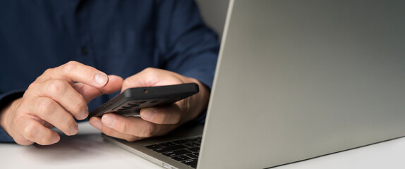 Close-up of hands using smartphone with laptop on desk showing modern digital lifestyle and connectivity