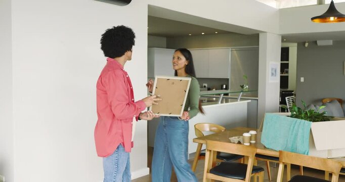 Carrying frame into home Diverse couple marking spot hammering nail hanging it dancing to celebrate