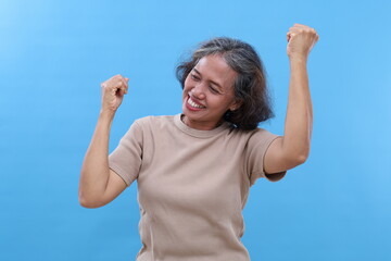 Portrait of attractive and cheerful gray-haired Asian old woman, smiling while dancing having fun and rejoicing, celebrating success or receiving good news, standing isolated on blue background.