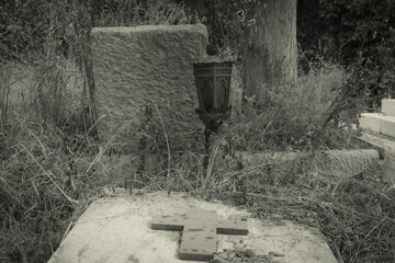 Black and white photo of an old grave with an old lamp  in cemetery.