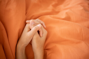 Couple holding hands under orange blanket on bed