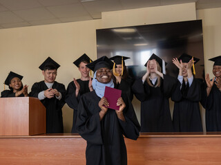 Happy African woman in hijab receiving diploma and classmates applauding her. 