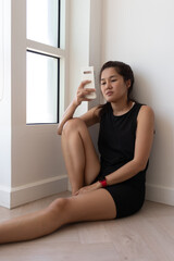 Naklejka premium Asian woman relaxing against wall while holding smartphone