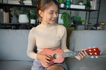 Asian woman in casual sits on sofa playing ukulele in living room