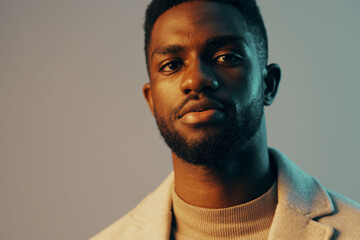 Obraz premium A confident young Black man in a stylish gray coat and beige turtleneck, portraying a sense of sophistication against a cool, gradient background