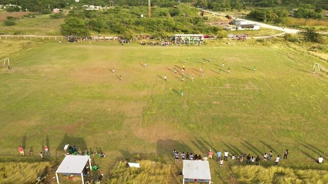 Vista a&eacute;rea de ni&ntilde;os jugando f&uacute;tbol infantil sobre c&eacute;sped en las afueras del pueblo