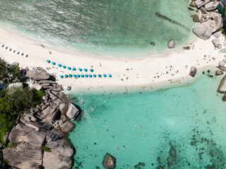 Sandy beach lined with umbrellas surrounded by clear turquoise waters and vibrant scenery. Thailand, Koh Tao.