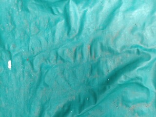 Wrinkled Green Plastic Tarp with Dirt Particles. A textured green tarp surface with wrinkles and...