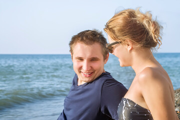 A young guy and a girl are talking on the beach against the background of the blue sea and blue sky on a sunny summer day
